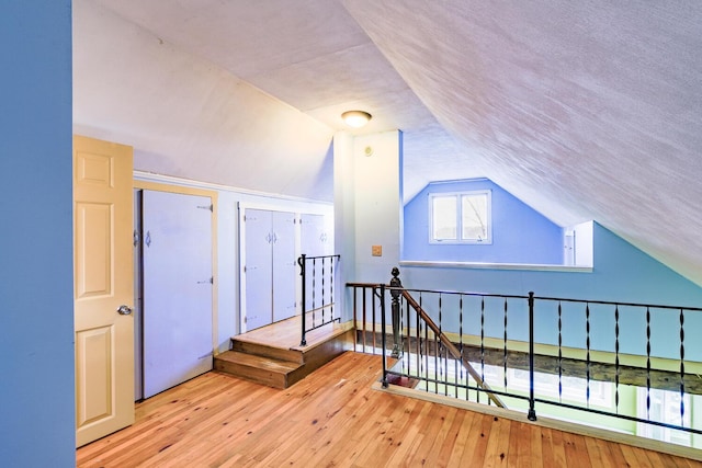 additional living space with a textured ceiling, light hardwood / wood-style flooring, and vaulted ceiling