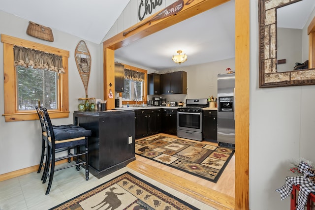 kitchen featuring sink, vaulted ceiling, appliances with stainless steel finishes, dark brown cabinetry, and a breakfast bar area