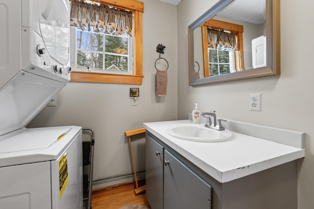 laundry room featuring light hardwood / wood-style flooring, stacked washing maching and dryer, sink, and a baseboard radiator