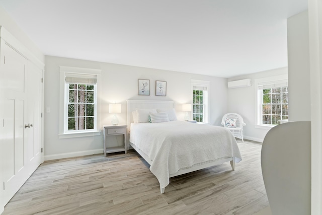 bedroom featuring a wall mounted AC, light hardwood / wood-style flooring, and multiple windows