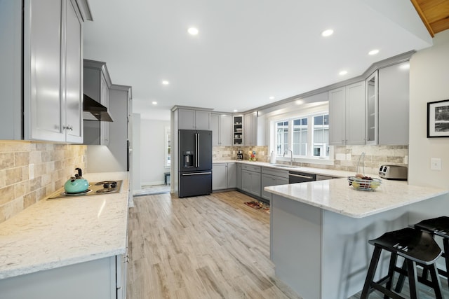 kitchen with light stone counters, gray cabinetry, high end black fridge, and wall chimney range hood