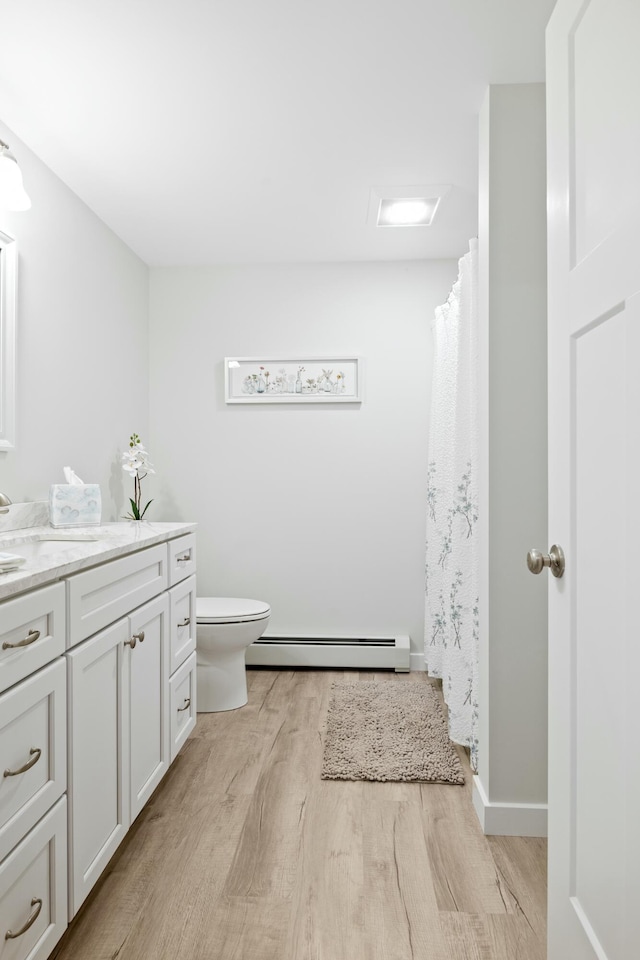 bathroom with toilet, vanity, a baseboard heating unit, and hardwood / wood-style flooring