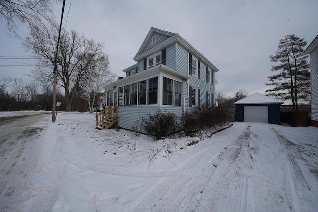 view of snow covered exterior featuring an outbuilding, a garage, and a sunroom