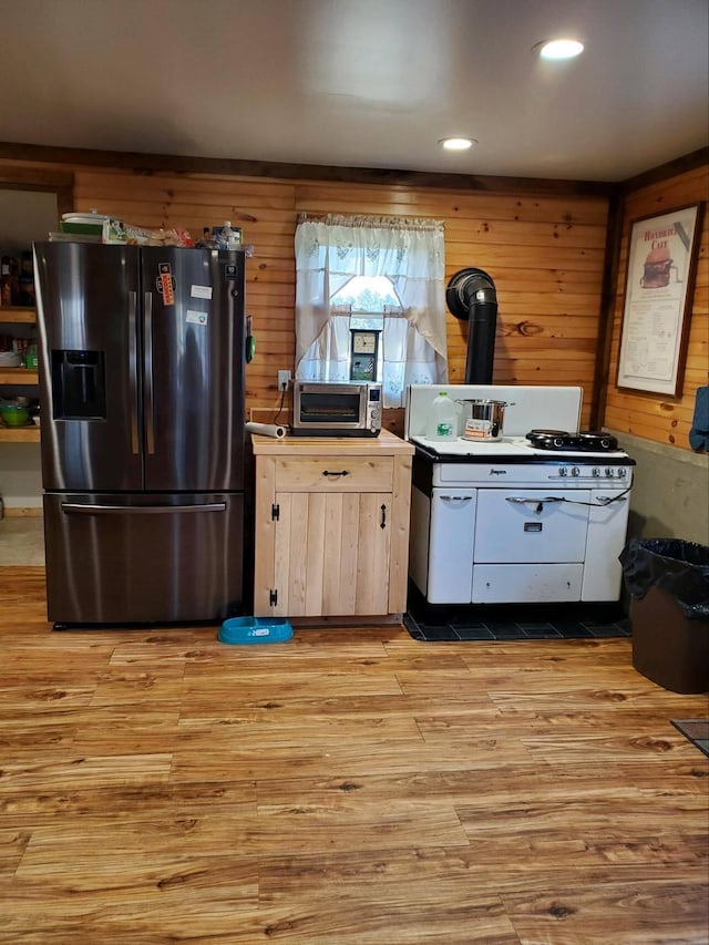 kitchen featuring light brown cabinetry, wooden walls, light hardwood / wood-style flooring, and stainless steel refrigerator with ice dispenser