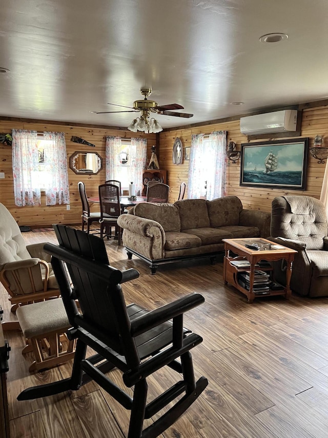 living room featuring hardwood / wood-style flooring, a wall unit AC, ceiling fan, and wood walls