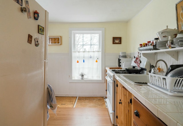 kitchen with tile counters, light hardwood / wood-style floors, and white stove