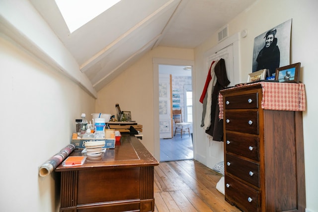 interior space with vaulted ceiling with skylight and light hardwood / wood-style floors