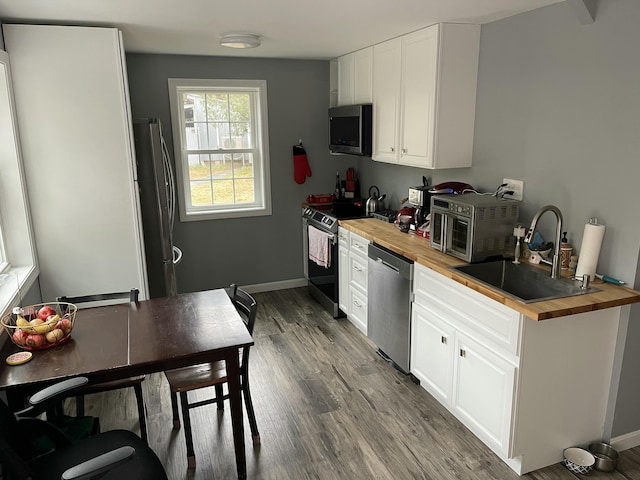 kitchen featuring white cabinets, sink, hardwood / wood-style flooring, butcher block counters, and stainless steel appliances