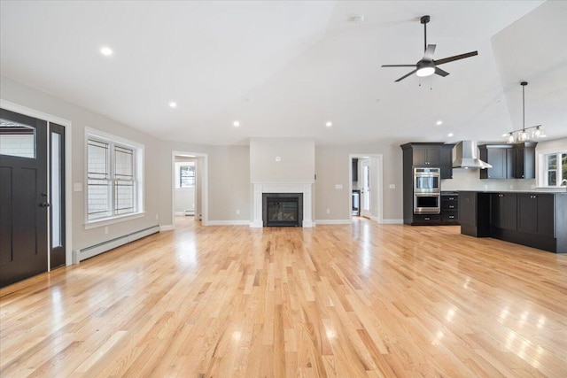 unfurnished living room featuring lofted ceiling, light wood finished floors, a baseboard heating unit, and a glass covered fireplace