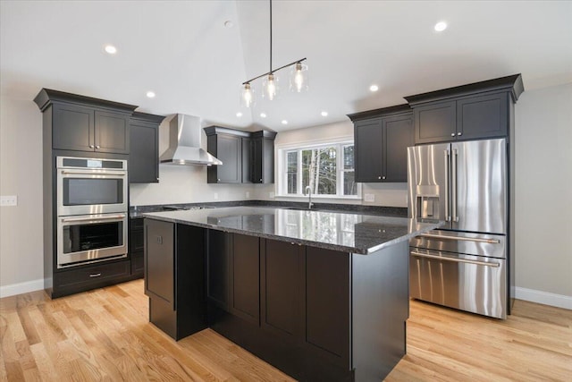 kitchen featuring appliances with stainless steel finishes, a kitchen island, wall chimney range hood, a sink, and dark stone counters