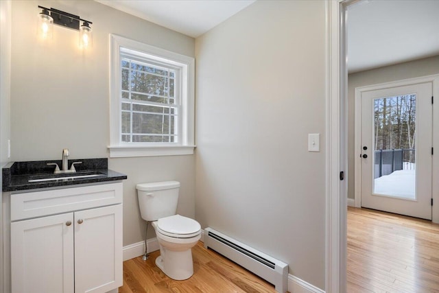 bathroom featuring a baseboard radiator, toilet, vanity, wood finished floors, and baseboards