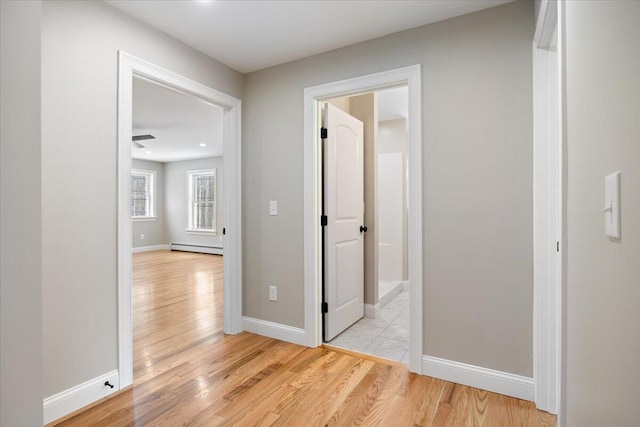 hallway featuring light wood-style flooring, a baseboard heating unit, and baseboards