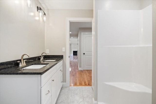 full bathroom with marble finish floor, double vanity, a sink, and baseboards