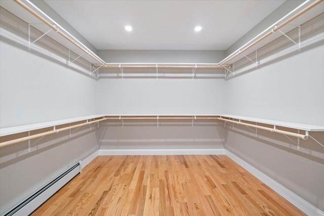 spacious closet with a baseboard heating unit and wood finished floors