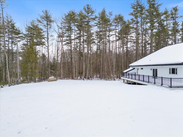 yard layered in snow with a deck and a wooded view