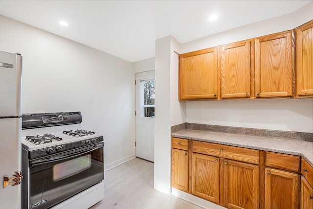 kitchen featuring white range with gas cooktop, stainless steel fridge, and light hardwood / wood-style flooring