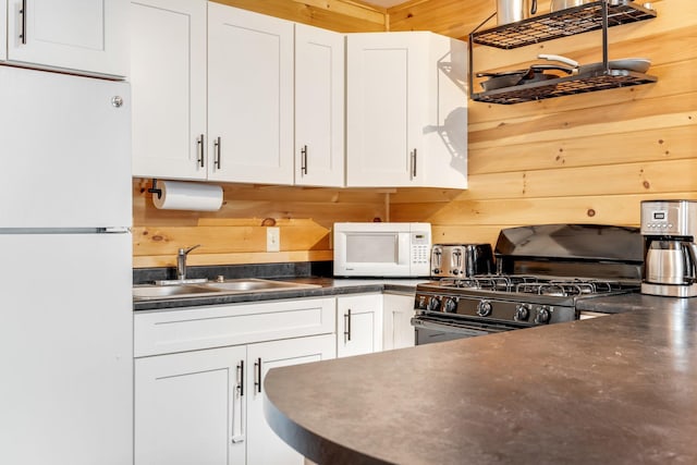 kitchen featuring white cabinetry, wood walls, sink, and white appliances