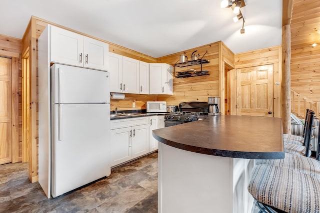 kitchen with kitchen peninsula, white appliances, white cabinetry, and wooden walls