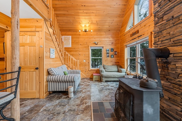 living room featuring wood walls, a wood stove, high vaulted ceiling, and a chandelier