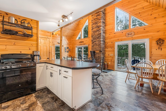 kitchen with kitchen peninsula, black range with gas stovetop, white cabinets, and wood walls