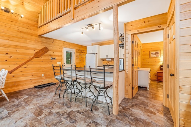 kitchen with a kitchen breakfast bar, rail lighting, white refrigerator, white cabinetry, and wood walls