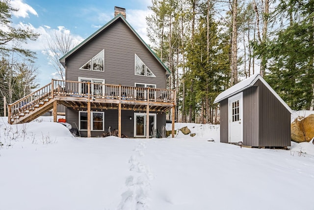 snow covered back of property featuring a wooden deck and a storage shed