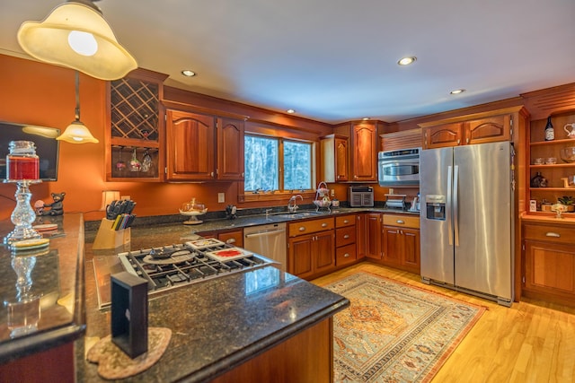 kitchen with sink, hanging light fixtures, dark stone countertops, light hardwood / wood-style floors, and stainless steel appliances