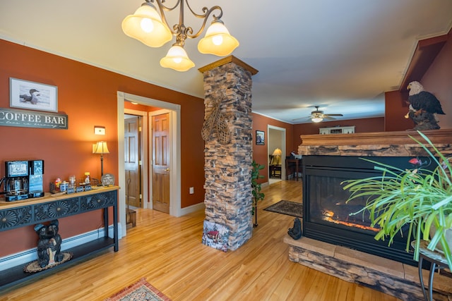 interior space with a fireplace, wood-type flooring, ceiling fan with notable chandelier, and ornate columns