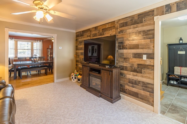 carpeted living room with ceiling fan, ornamental molding, and wooden walls