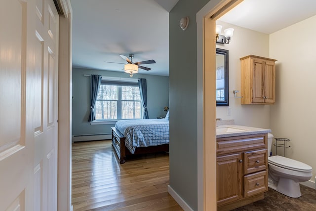 bedroom featuring ceiling fan, hardwood / wood-style floors, sink, and a baseboard heating unit