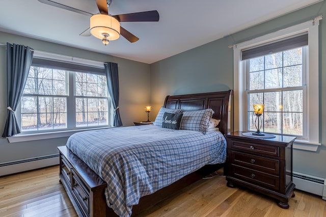 bedroom with multiple windows, light hardwood / wood-style floors, ceiling fan, and a baseboard heating unit