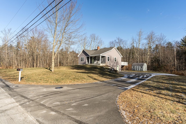 view of front of house featuring covered porch, a front lawn, and a storage shed