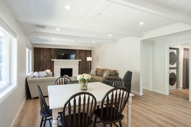 dining area featuring stacked washer / dryer, wooden ceiling, light hardwood / wood-style floors, beamed ceiling, and a brick fireplace