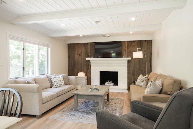 living room featuring a brick fireplace, light wood-type flooring, and beamed ceiling