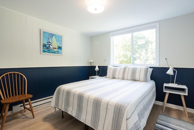 bedroom featuring baseboard heating, hardwood / wood-style floors, and wood walls