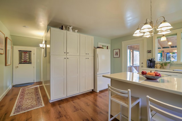 kitchen featuring white cabinets, white refrigerator, hanging light fixtures, wood-type flooring, and a chandelier