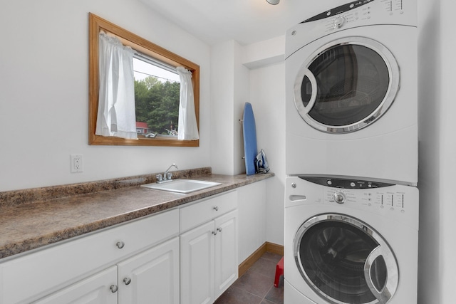 clothes washing area with cabinets, dark tile patterned floors, stacked washer / dryer, and sink