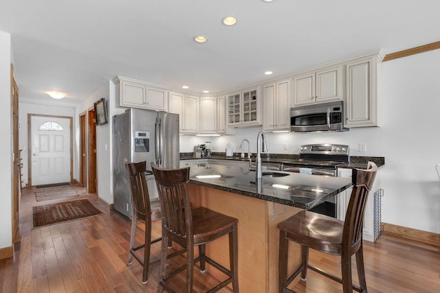 kitchen with stainless steel appliances, dark wood-type flooring, sink, dark stone countertops, and a breakfast bar area