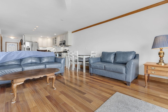 living room with crown molding, sink, and light hardwood / wood-style floors