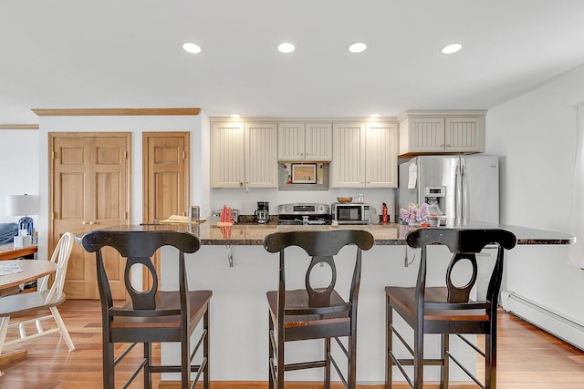 kitchen featuring light hardwood / wood-style floors, a kitchen bar, appliances with stainless steel finishes, and a baseboard radiator