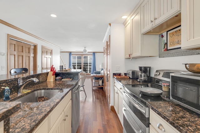 kitchen featuring appliances with stainless steel finishes, dark stone counters, sink, cream cabinetry, and dark hardwood / wood-style floors