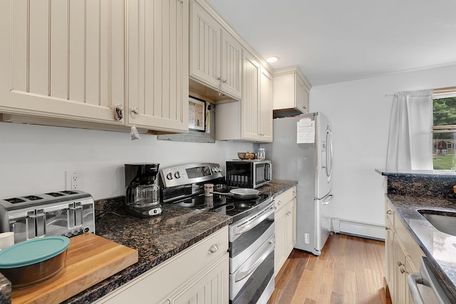 kitchen with dark stone counters, light hardwood / wood-style flooring, stainless steel appliances, and a baseboard radiator