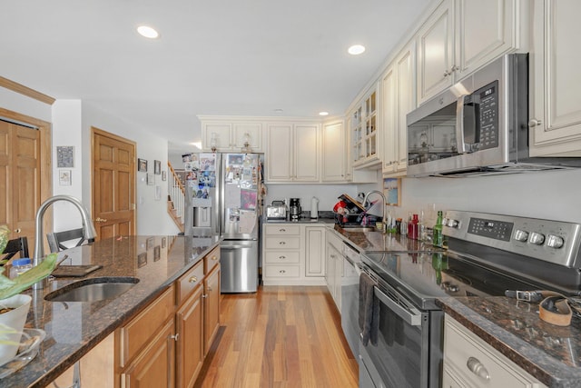 kitchen with stainless steel appliances, light hardwood / wood-style floors, dark stone countertops, and sink