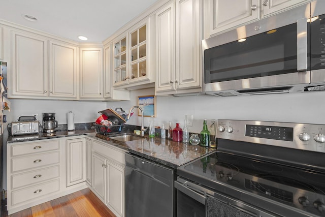 kitchen with appliances with stainless steel finishes, light hardwood / wood-style flooring, dark stone counters, and sink