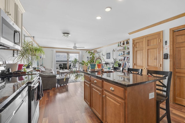 kitchen with appliances with stainless steel finishes, dark hardwood / wood-style flooring, a kitchen island with sink, and a kitchen breakfast bar