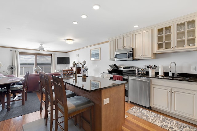 kitchen featuring light wood-type flooring, stainless steel appliances, a kitchen island with sink, sink, and cream cabinetry