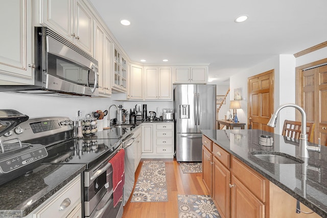 kitchen with dark stone counters, white cabinets, sink, light hardwood / wood-style floors, and stainless steel appliances