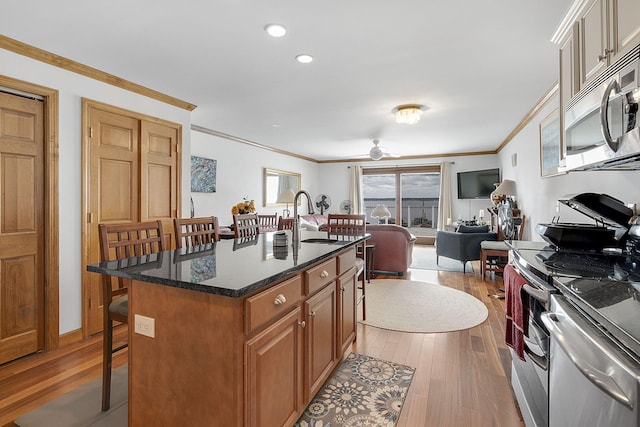 kitchen with ornamental molding, stainless steel appliances, a center island with sink, dark stone countertops, and light hardwood / wood-style floors