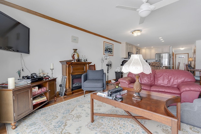 living room with a fireplace, light hardwood / wood-style flooring, ceiling fan, and crown molding