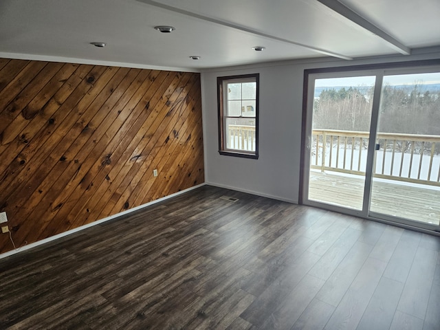 empty room featuring beam ceiling, dark wood-type flooring, and wood walls